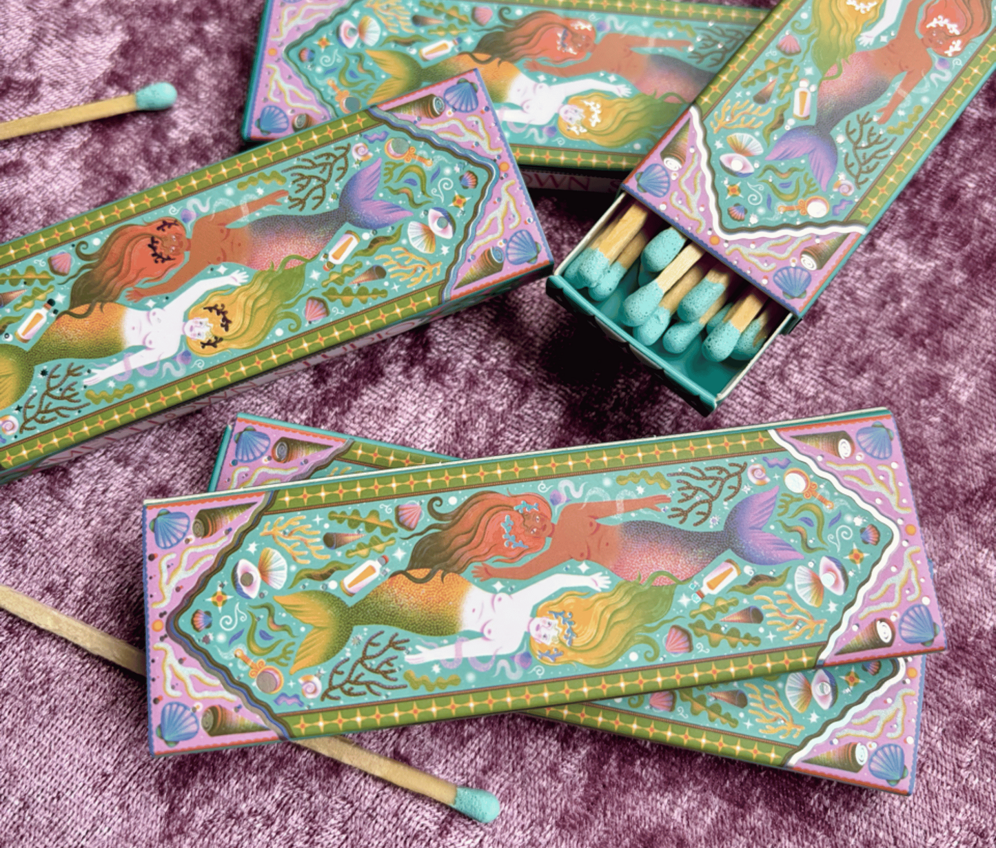 Matchboxes with mermaid design on a purple textured surface
