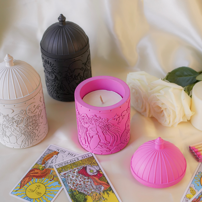 Pink candle with embossed design on a surface with tarot cards and flowers.
